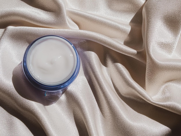 Foto modello di barattolo di crema di vetro blu su tessuto di seta liscio alla luce solare crema idratante naturale per la cura della pelle cosmetica