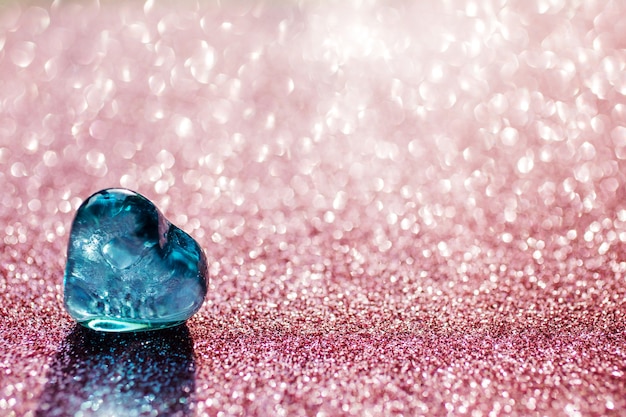 Photo blue glass heart on the shining pink bokeh background. focus on the left bottom on the heart. valentines day. light shines through the heart. greeting card, copy space.