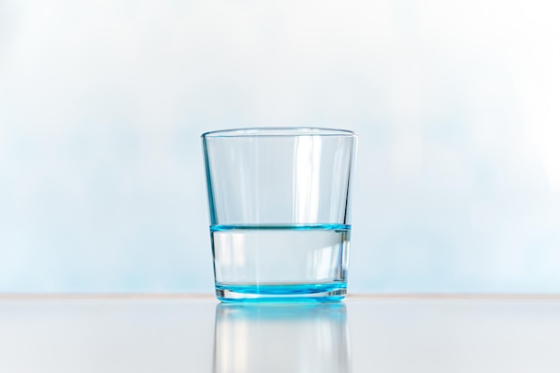 Blue glass with clear water on a blue background clear and full glass of water