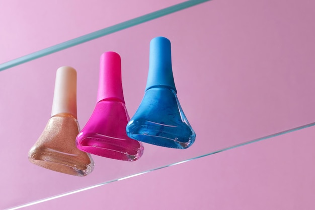Blue gold and pink nail polish in glass tubes stand on a glass surface on a pink background