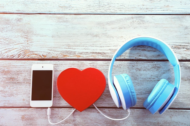 Blue headphones with heart and phone on wooden background