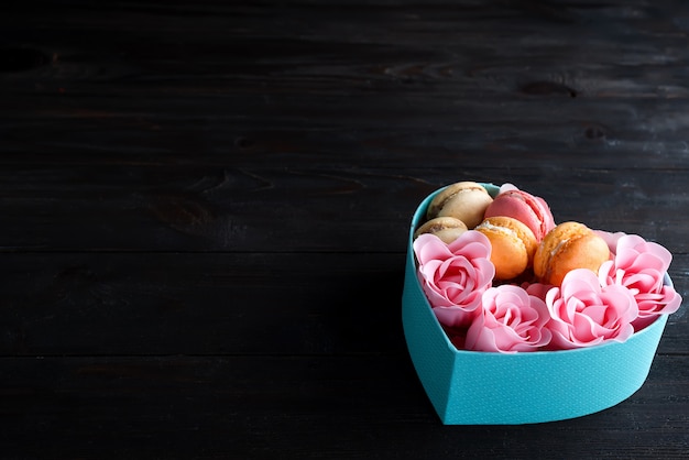 Blue heart box with macaroons and Rose on dark wooden background, copy space