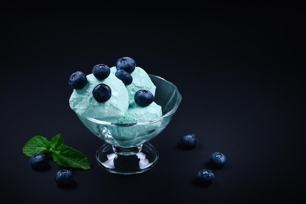 Blue ice cream in cup with blueberry fruits and mint on black background.