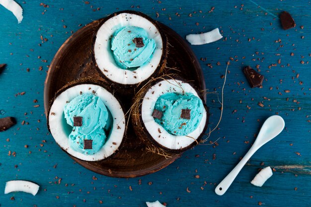 Blue ice cream with chocolate in coconut bowl on wooden surface. Summer food. Top view. Copy space.