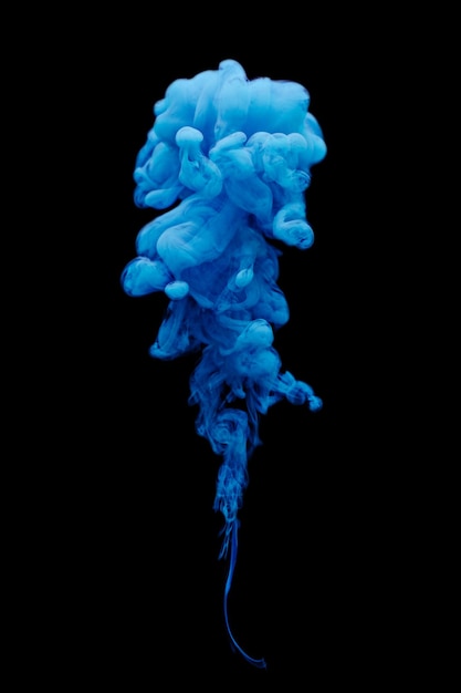 Photo blue ink swirling in water isolated on black background