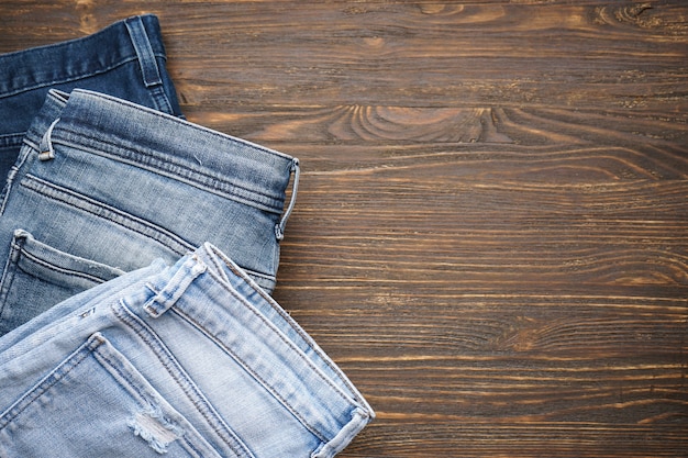 Blue jeans on brown wooden background, top view. Space for text.