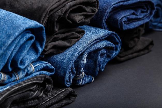 Фото Синие джинсы, свернутые в рулоны, лежат на черном фоне. черно-синие джинсовые брюки в виде рулонов.