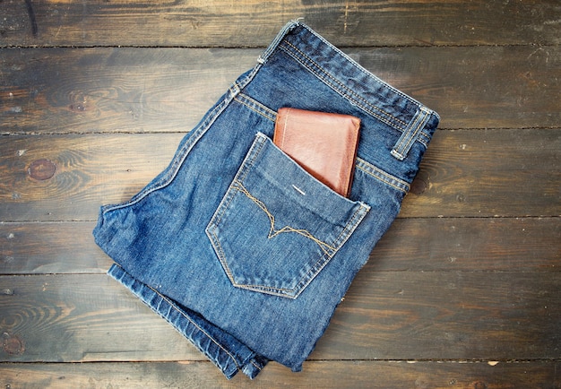 Blue jeans and leather wallet on wooden background