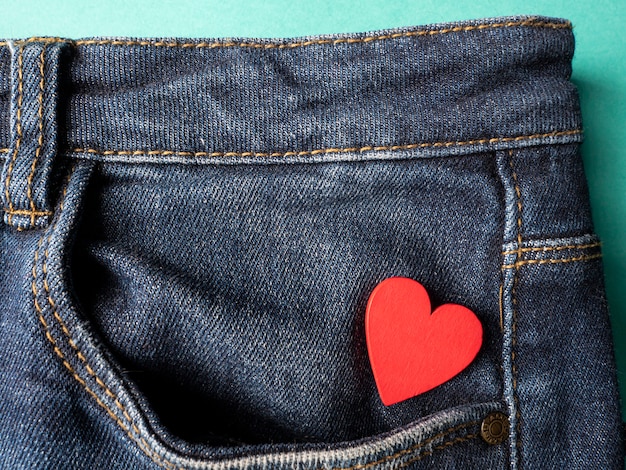 Blue jeans and one red heart lies in the back pocket of jeans on green