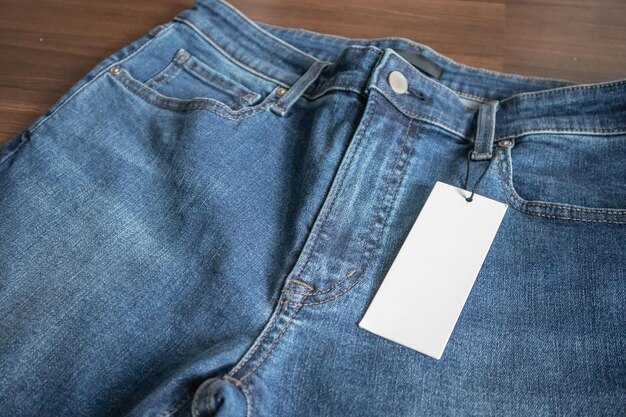 Blue jeans with blank white price label tag on wooden background