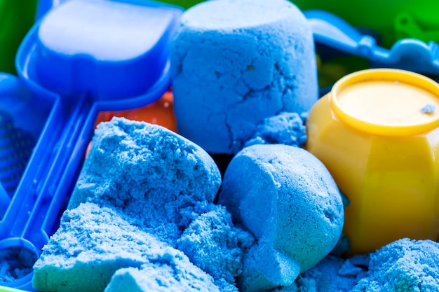 Blue kinetic sand with a small plastic shovel and toys lies in the container