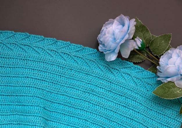 A blue knitted fabric lies on a gray background next to a blue rose flower