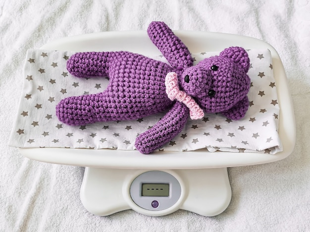 A blue knitted teddy bear lies on an electronic baby scale on a diaper with stars