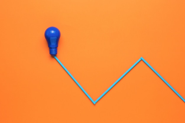 A blue lamp and an imitation of a connected wire on an orange background. Minimalism. The concept of energy and business. Flat lay.