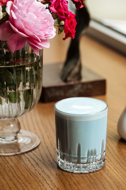 Blue lavander latte beverage in a glass on the table with flowers