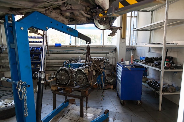 Photo blue lift crane with car engine in auto service workshop