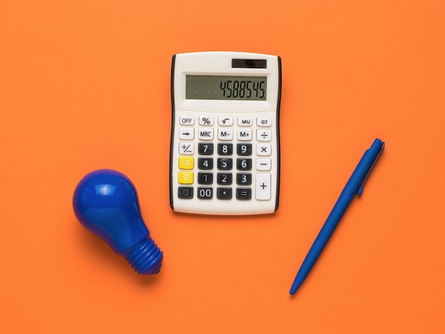Синяя лампочка, синяя ручка и калькулятор на оранжевом фоне.
