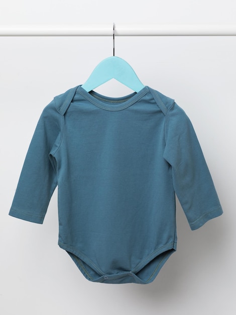 A blue longsleeved baby jumpsuit hangs on a hanger on a light background