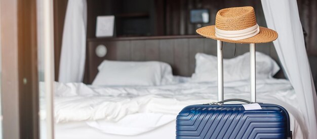 Blue Luggage with hat in modern hotel room after door opening. Time to travel, service, journey, trip, summer holiday and vacation concepts