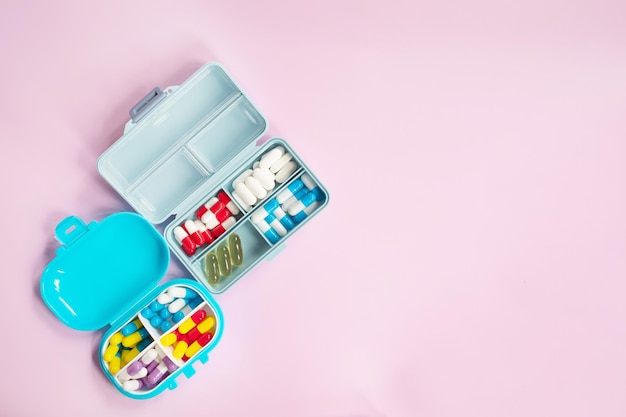 A blue lunch box with a box of medicine on a pink background.