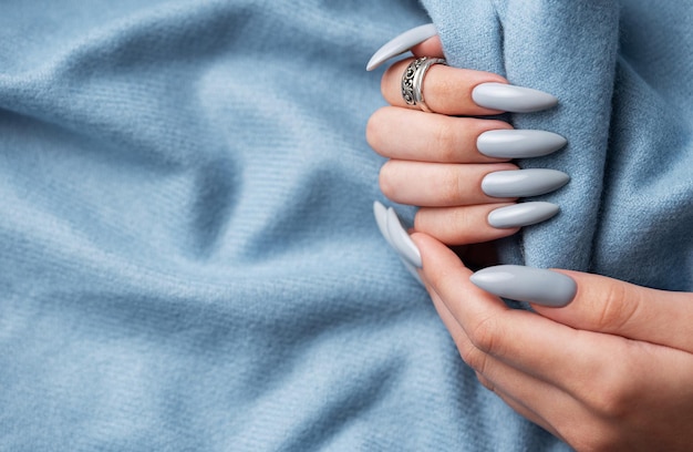 Blue manicure nails with a blue scarf Female hand with blue nail design Woman hand on blue fabric