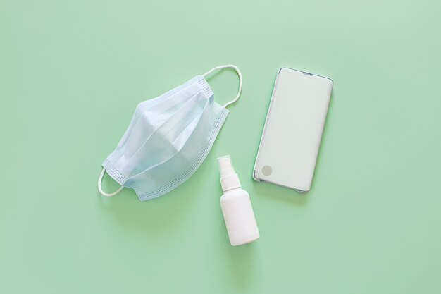 blue medical mask, smartphone and liquid antimicrobial spray bottle.