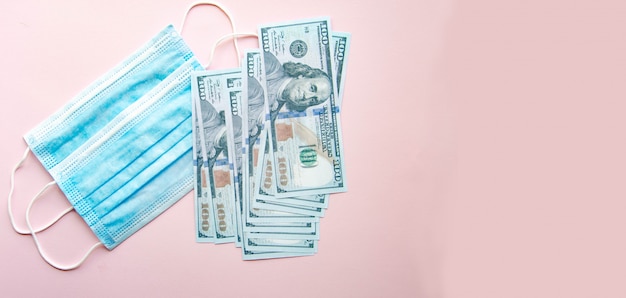 Photo blue medical mask with dollars on a pink background.