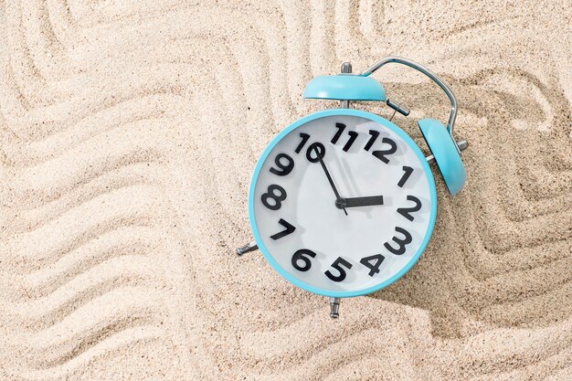 Blue metal alarm clock on sand background, top view with copy space