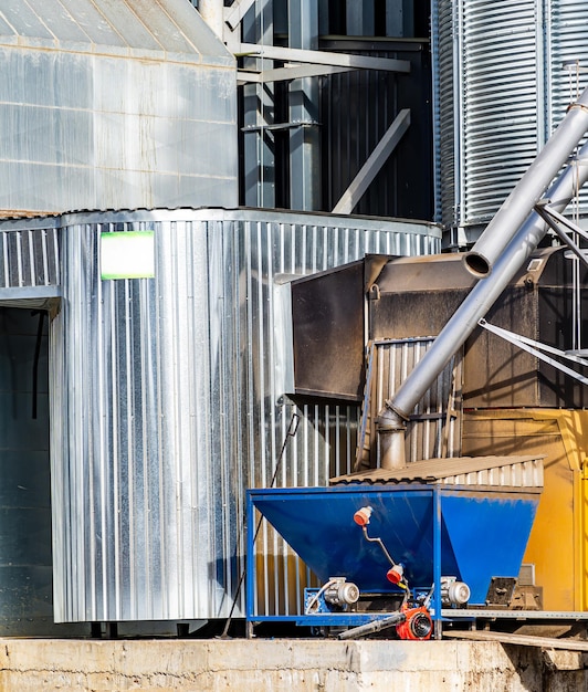 Blue metal grain cart is parked next to large metal silo