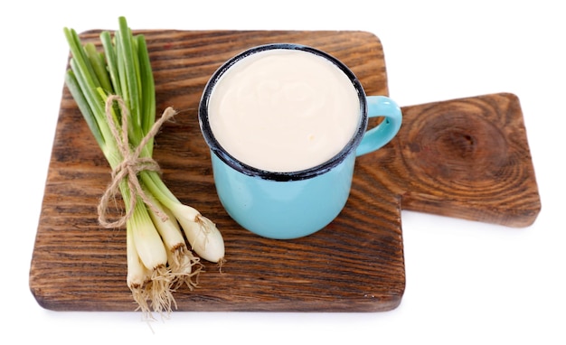 Blue metal mug with cream and onion on a wooden cutting board on white background isolated