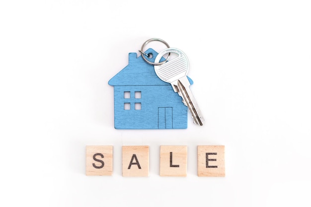 Photo blue mini house figure with keys on an isolated white background. wooden letters inscription sale