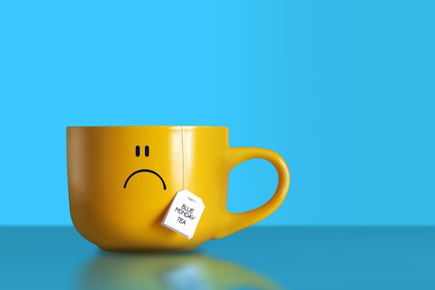 Blue monday tea text with sad smiley face on big yellow cup on blue background. Copy space.