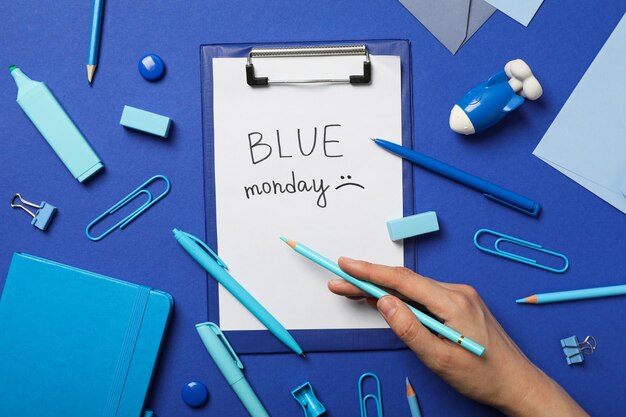 blue monday text stationery and hand with pencil on blue background top view