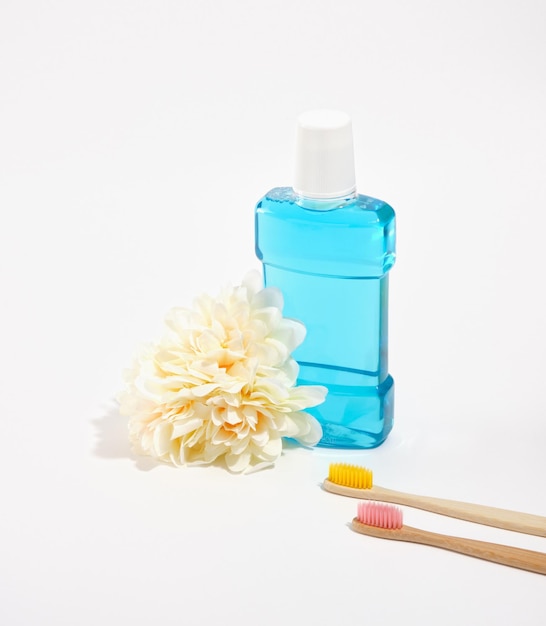 Blue mouthwash and organic bamboo toothbrushes with colorful bristles isolated Fresh lush flower