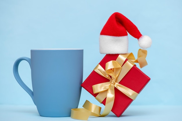 Blue mug with a christmas gift and a hat on a blue background