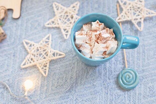 Blue mug with cocoa marshmallows blue lollipop against the background of christmas decor