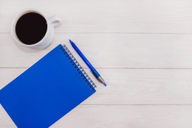 Blue notebook with a pen and a cup of coffee on a white 