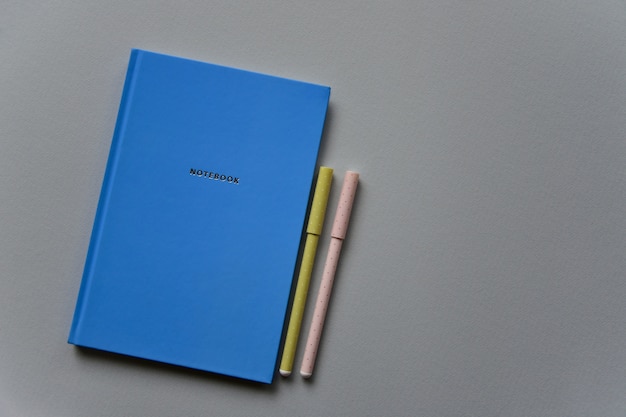 Photo blue notebook with two pens on a gray paper background. top view. close-up. flat lay.