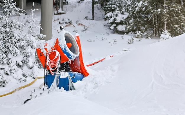 Blue and orange snow making cannon, some trees in background.