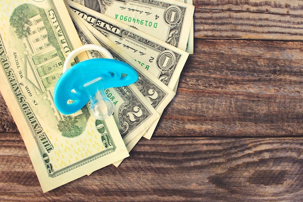 Blue pacifier on the background of money. Toned image.