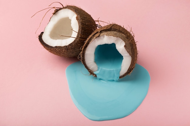 Blue paint flowing from coconut half on pink table. Creative background with copy space, bold design for poster or clothing print