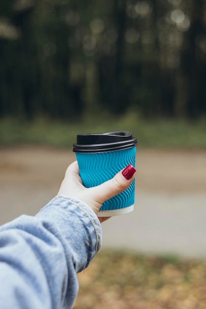 blue paper cup with coffee in woman hand on blurred nature background