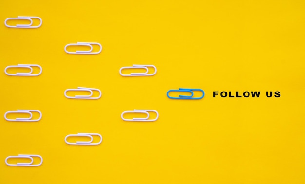 Blue paperclip leads white paperclips with the follow us message Social media or internet followers