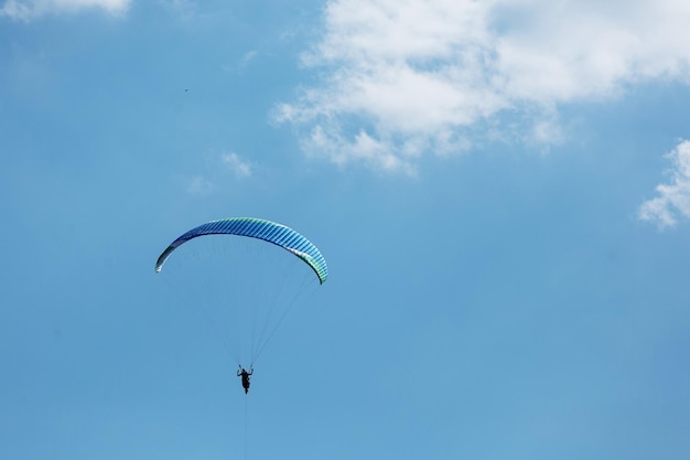 Blue Paraglider flying into the sky with clouds on a sunny day