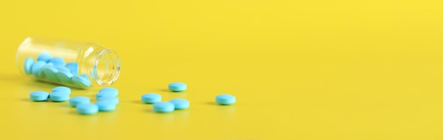 Blue pills are poured out of a glass bottle on a yellow background Healthcare medical pills