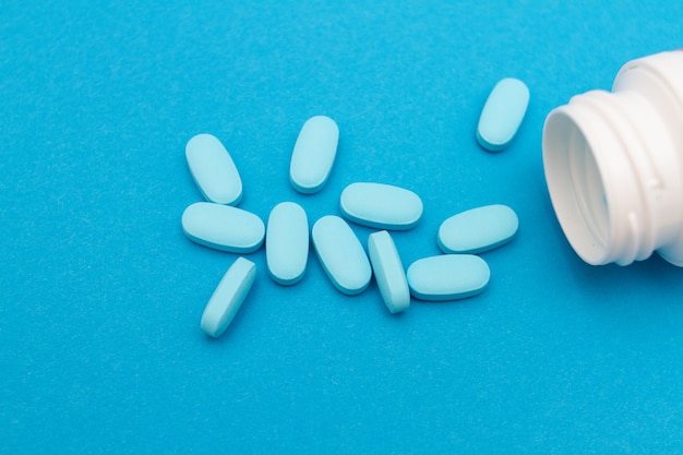 Blue pills an pill bottle on blue background