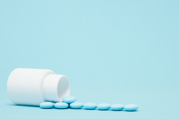 Blue pills and pill bottle on blue background