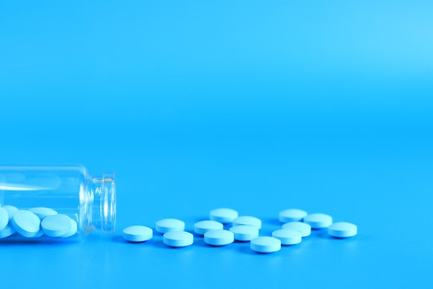 Blue pills poured out of a glass bottle on a blue background Vitamin B complex side view copy space