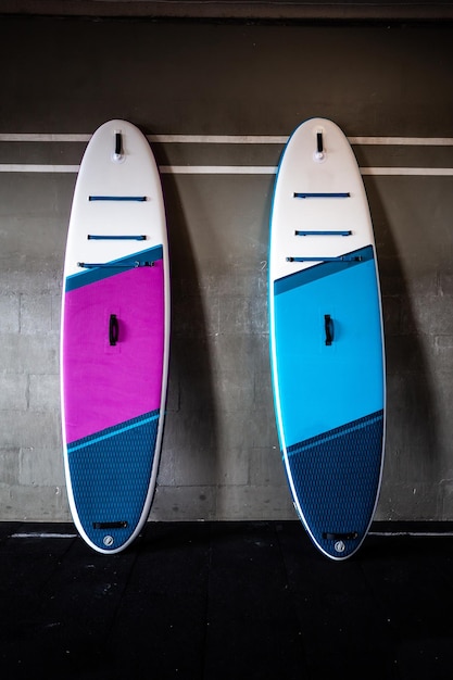 Синие и розовые стоячие доски для гребли SUP у стены Оборудование для серфинга и супбординга вблизи