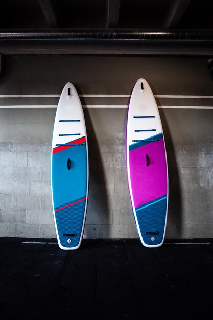 Синие и розовые стоячие доски для гребли SUP у стены Оборудование для серфинга и супбординга вблизи